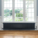 Radiatore tradizionale a 4 colonne in grigio antracite, con finitura liscia, posizionato sotto una grande finestra in legno chiaro