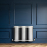 Radiatore tradizionale orizzontale a 4 colonne, 600 x 785 mm, di colore bianco, installato su una parete blu elegante con dettagli in legno chiaro