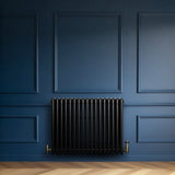 Radiatore tradizionale orizzontale a 4 colonne, 600 x 785 mm, finitura nera lucida su parete blu, con dettagli in ottone