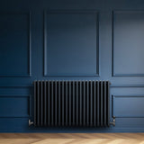 Radiatore tradizionale a 4 colonne orizzontale, colore antracite, installato su una parete blu scuro con pavimento in legno chiaro