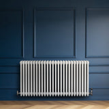 Radiatore tradizionale orizzontale a 4 colonne, 600 x 1190 mm, finitura bianca lucida, installato su parete blu scuro, elegante e moderno