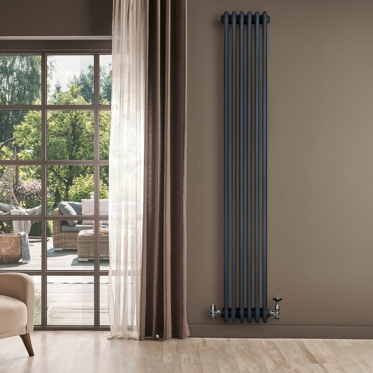 Radiatore tradizionale verticale a 4 colonne, colore antracite, installato su parete beige, con finestre che mostrano un giardino verde