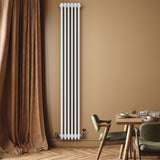 Radiatore tradizionale verticale a 4 colonne, finitura bianca, installato su parete color beige, accanto a tavolo elegante e sedie verdi