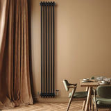 Radiatore tradizionale verticale a 4 colonne, finitura nera lucida, installato su parete beige, accanto a tavolo in legno e sedie verdi