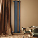 Radiatore tradizionale verticale a 4 colonne, finitura antracite, installato su parete beige, accanto a tavolo e tende marroni