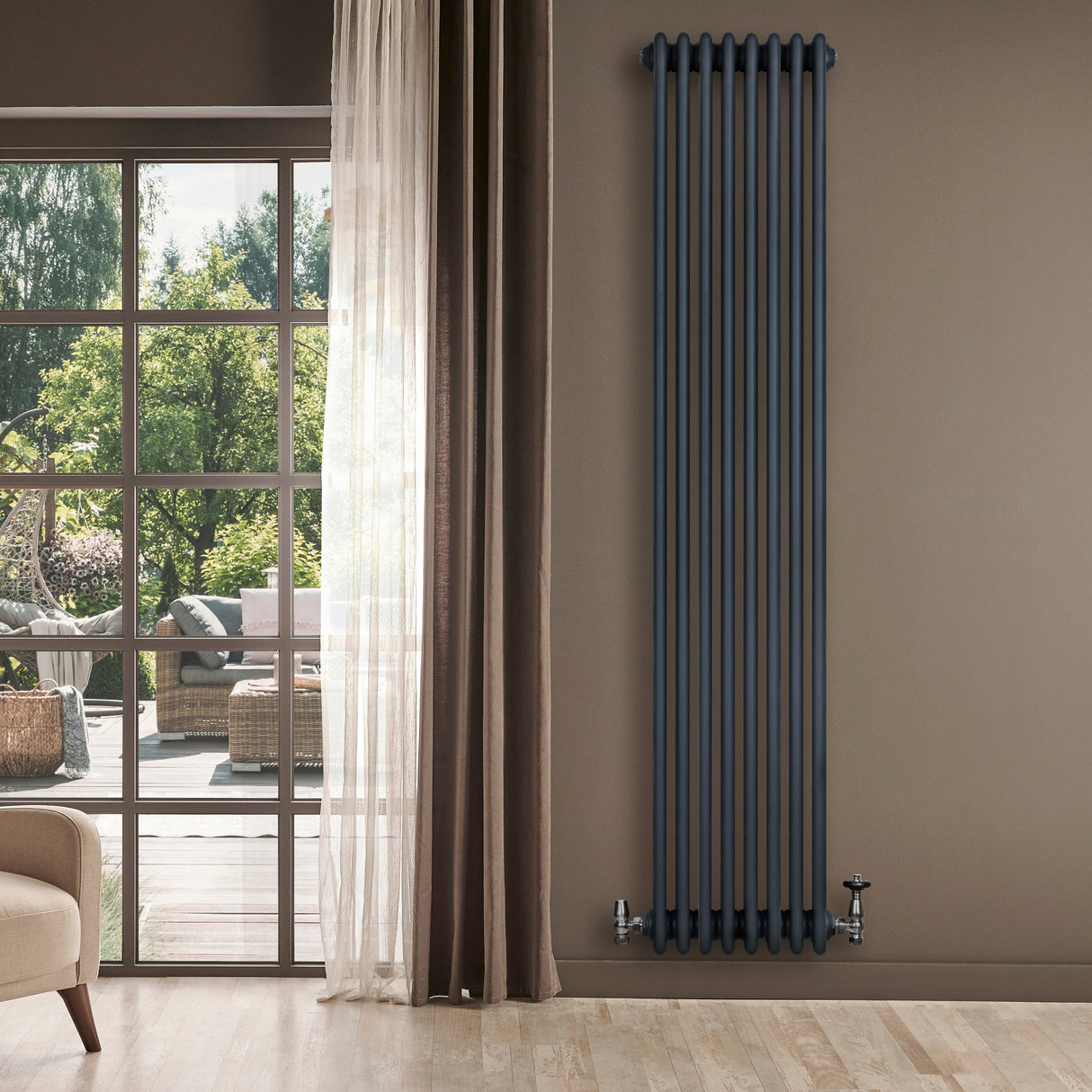 Radiatore tradizionale verticale a 4 colonne, colore antracite, installato su parete beige vicino a una finestra con vista esterna