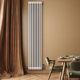 Radiatore tradizionale verticale a 4 colonne, bianco, installato su parete beige, accanto a tavolo e sedie moderne in legno