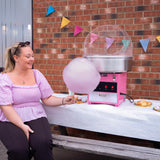 Macchina per zucchero filato rosa con una donna che tiene una grande nuvola di zucchero filato viola, decorazioni colorate sullo sfondo